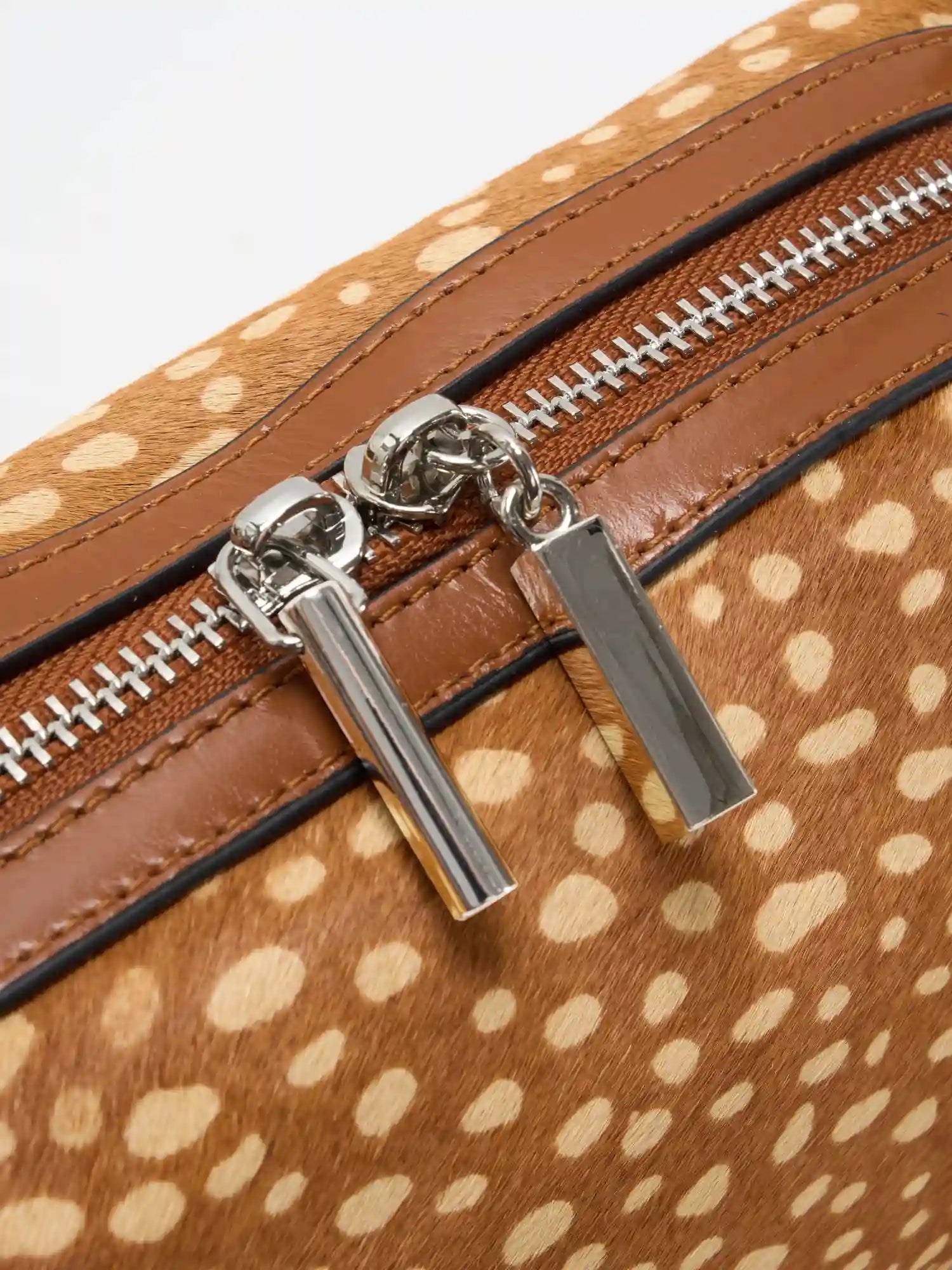 Close-up of silver-tone dual zipper pulls and cowhide trim
