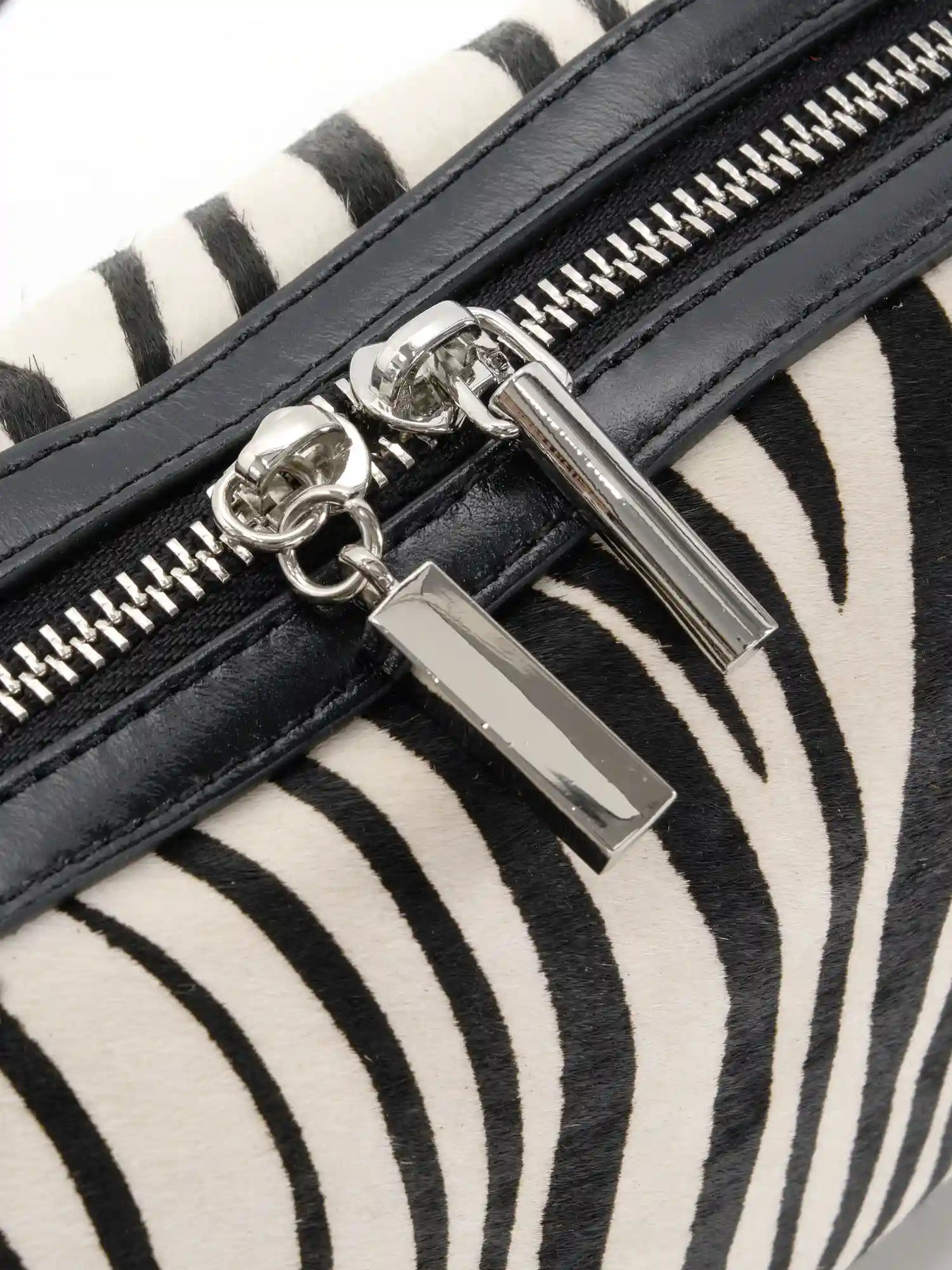 Close-up of silver-tone dual zipper pulls and black cowhide trim