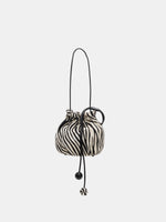 Zebra-print bag suspended by the shoulder strap with long spherical drawstring ends