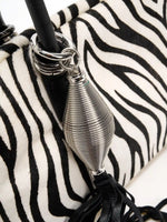Bright silver tassel charm and stacked handle rings on zebra hide