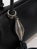 Bright silver sculptural tassel charm against fine-grain black leather