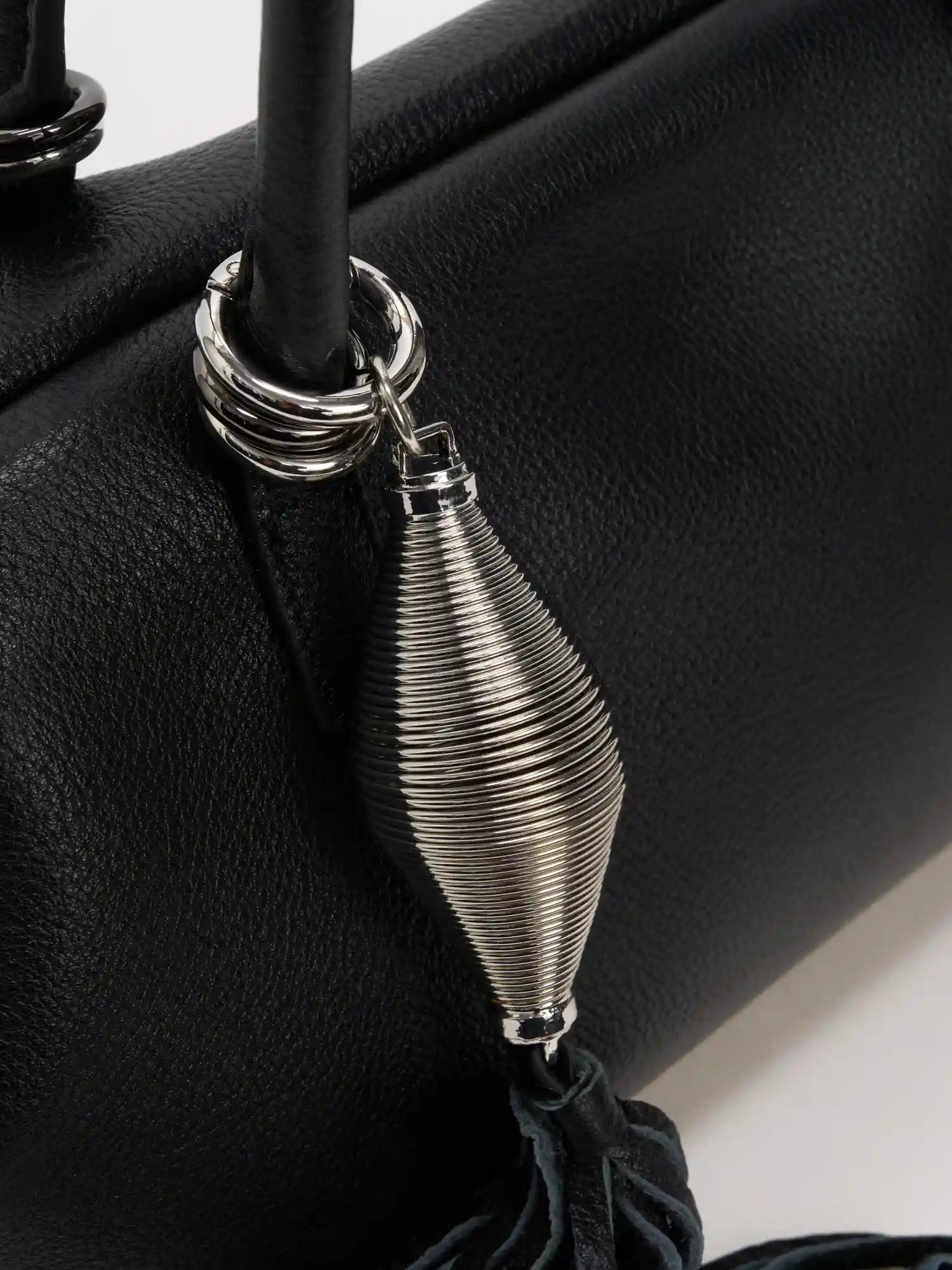 Bright silver sculptural tassel charm against fine-grain black leather