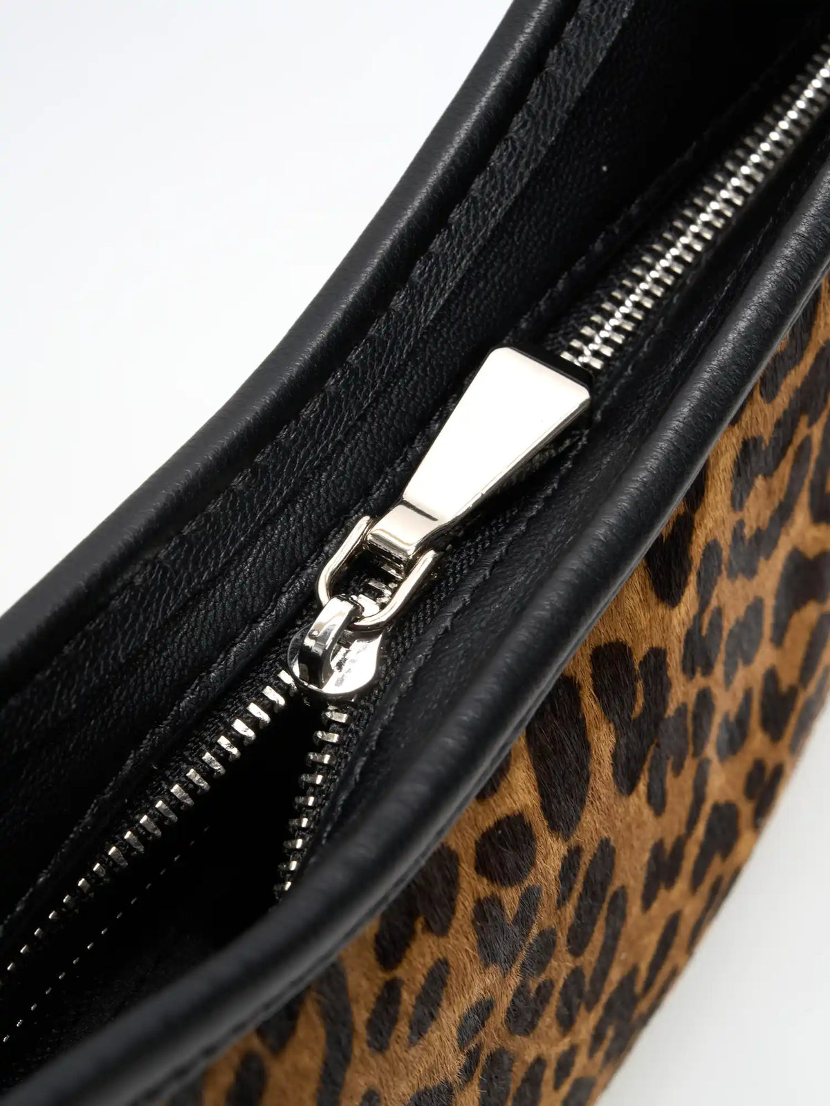 Close-up of the metal zip pull and black trim on the leopard crescent bag