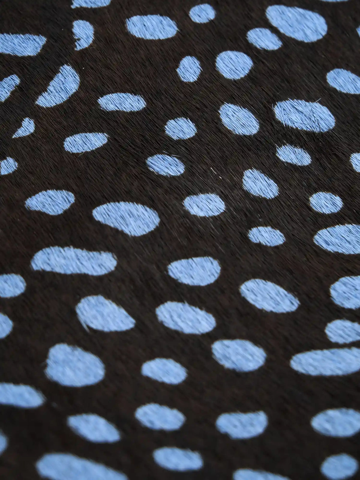 Close-up of irregular pale blue spots on the dark hair-on hide surface