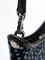 Close-up of the metal strap clasp and black trim on the blue-spotted crescent bag