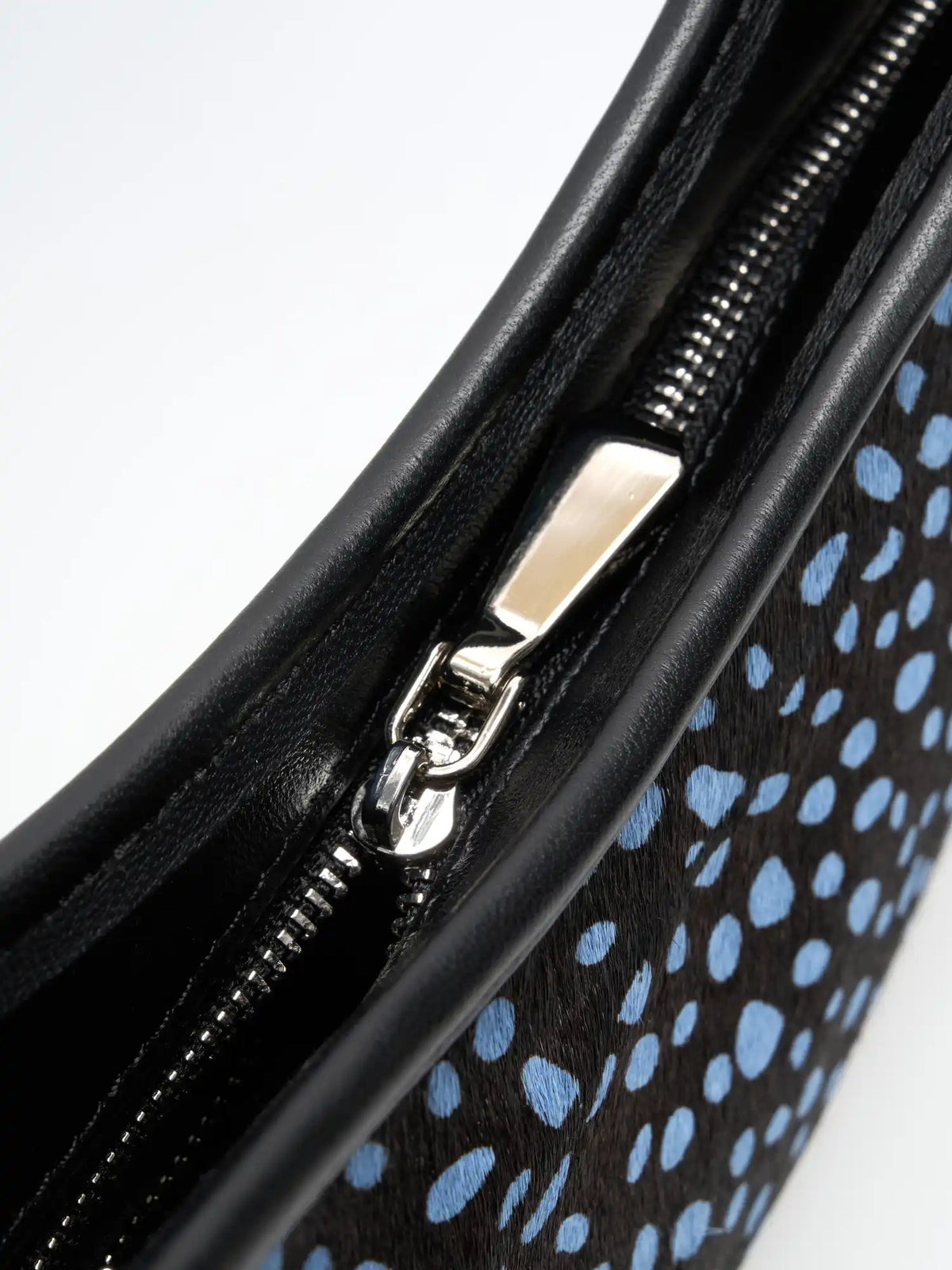 Close-up of the metal zip pull and black trim on the blue-spotted crescent bag