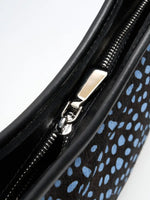 Close-up of the metal zip pull and black trim on the blue-spotted crescent bag