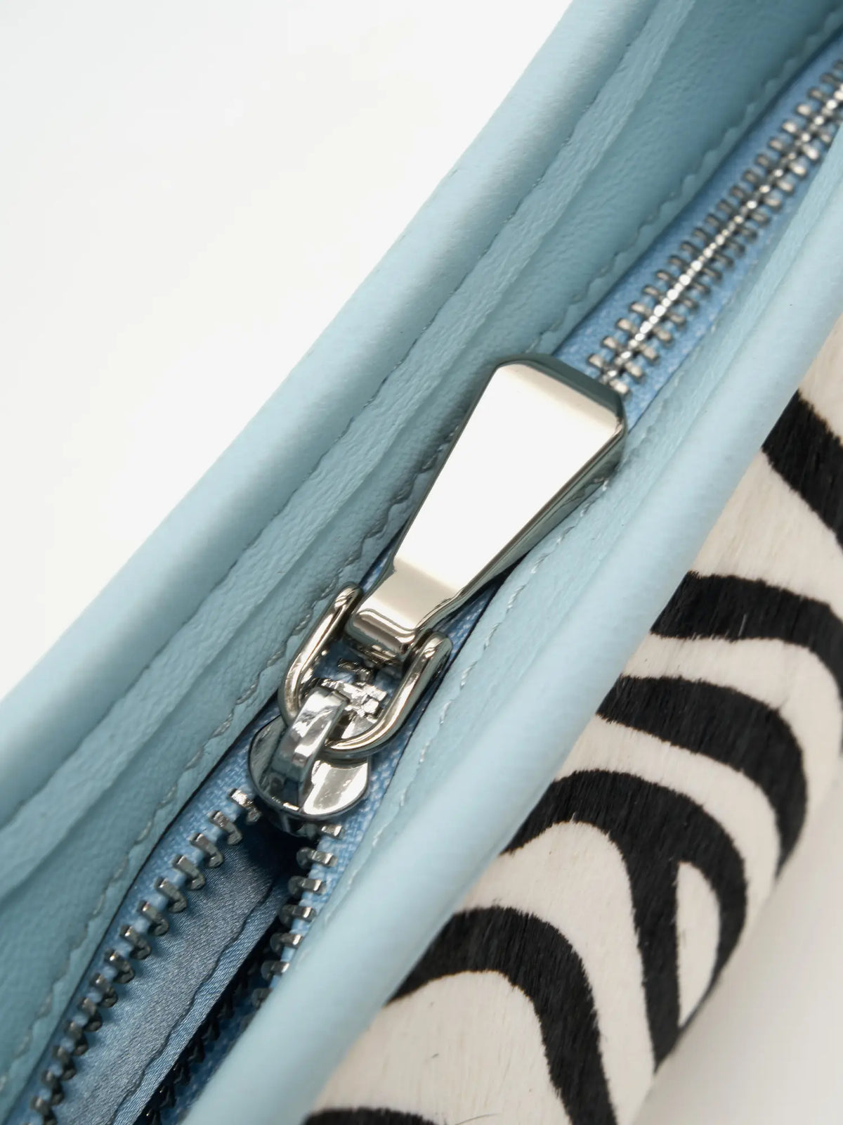 Close-up of the metal zip pull and ice-blue trim on the zebra crescent bag