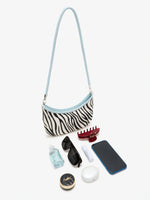 Ice Zebra crescent bag beside a phone, sunglasses, hair clip, earbuds case, and small beauty items
