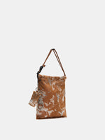 Angled view of Gilded Caramel bucket bag showing the tall silhouette and hanging accessories