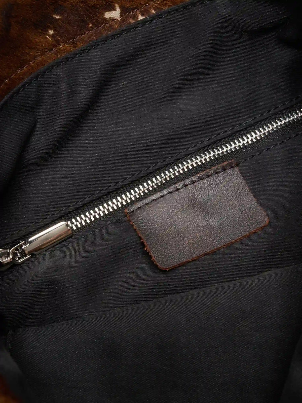 Black fabric lining and interior zip pocket with brown leather tab inside Mocha Cow Print bag
