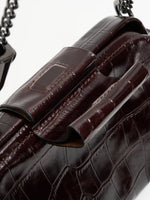 Burgundy Croc cowhide chain baguette bag close-up of the matching magnetic tab and framed top